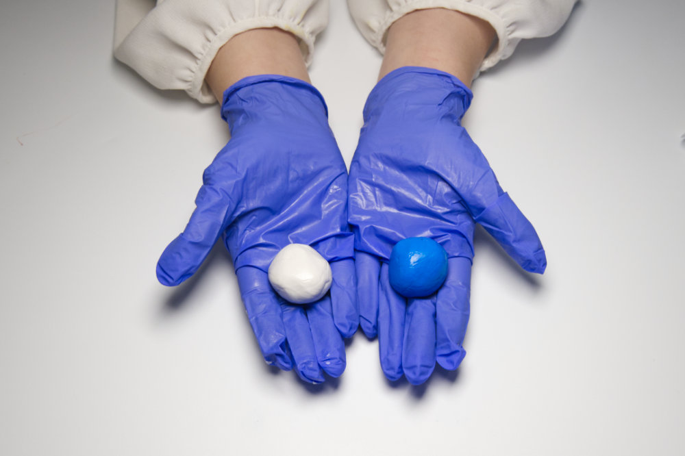 A woman's hands wearing gloves holding Smiles Club oral impression putty in her hands.