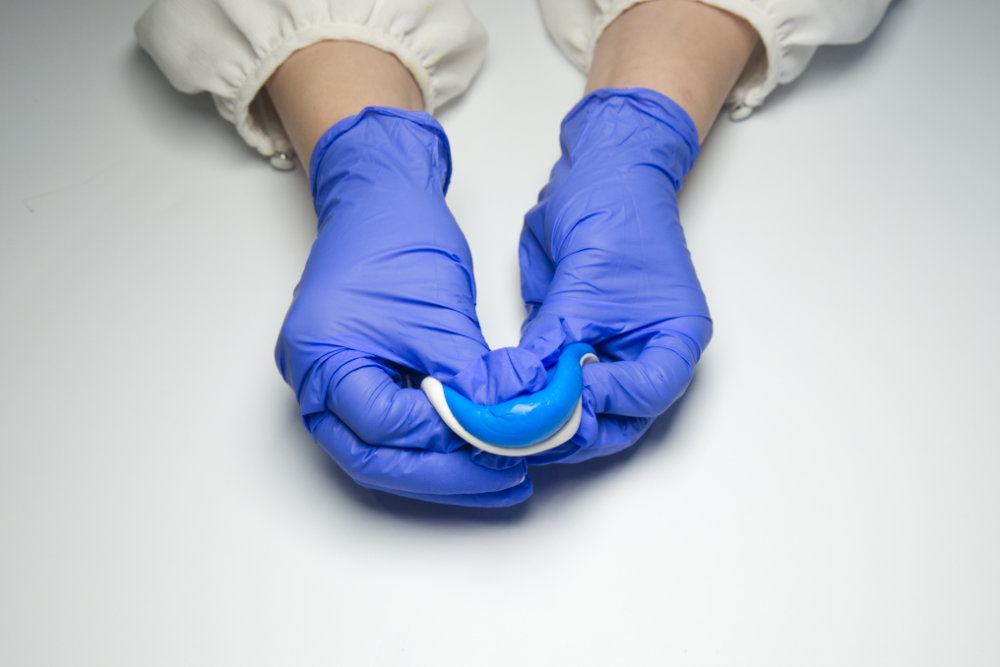 A woman's hands wearing gloves mixing Smiles Club oral impression putty in her hands.